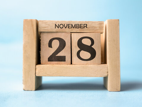 A wooden block calendar for November 28th on a light blue background.