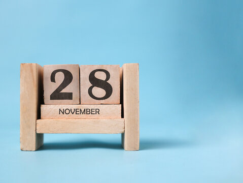 A wooden block calendar for November 28th on a light blue background.