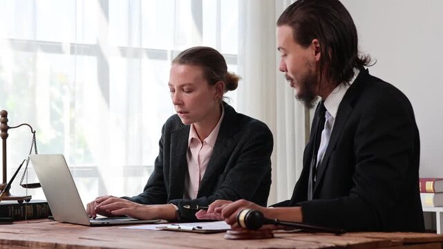 Professional lawyers collaborating on legal case using laptop in office with judge gavel and scales of justice
