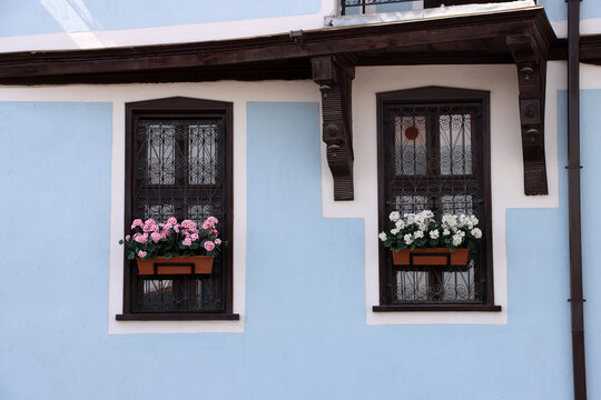 There are colorful flowers in front of small wooden windows. A view of architectural details from a Turkish house.