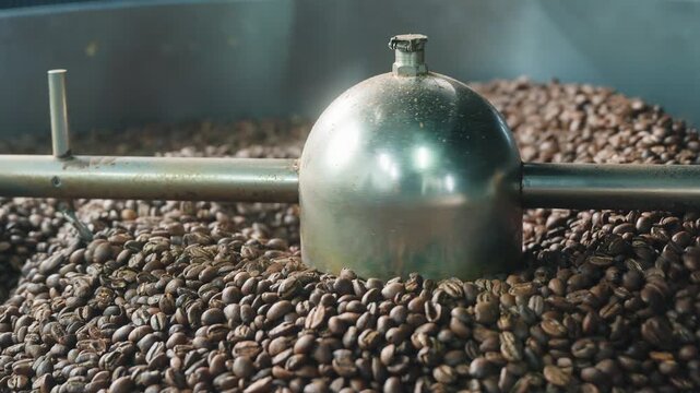 Close up roasted coffee beans blending inside factory industrial drum mixer roaster machine stirring grains during caffeine aroma production roasting process working equipment beverage preparation