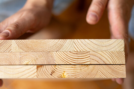 Close up of hands touching the cut edge of a pine wooden plank showing natural grain texture. The image highlights raw timber quality and craftsmanship in a handmade diy furniture project.
