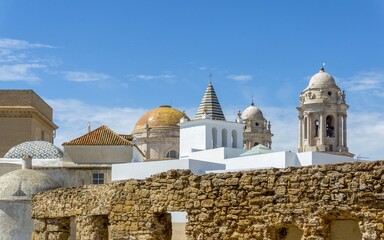 Historic buildings of Cádiz city featuring the iconic golden dome and bell towers of the Cathedral rising above traditional rooftops and an ancient stone wall © photoopus