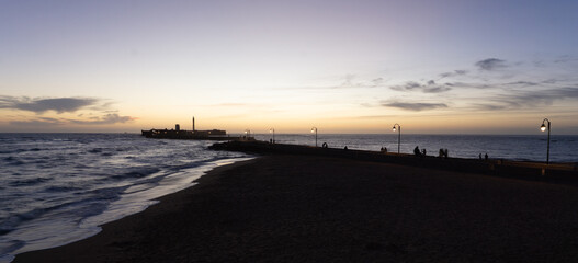 People enjoying the tranquil sunset at La Caleta Beach in Cádiz, with the iconic San Sebastián Castle silhouetted against the colorful evening sky and gentle waves reaching the shore © photoopus