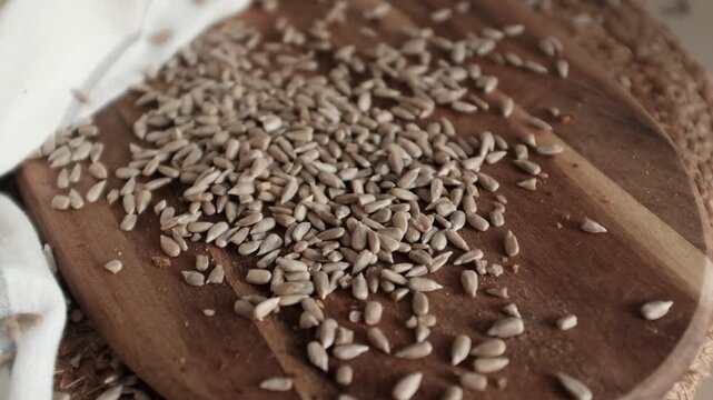 Peeled sunflower seeds scattered on a rustic wooden board next to a kitchen towel. This footage is ideal for healthy food blogs, organic snack commercials, and culinary recipe videos.