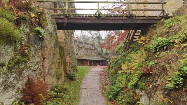 Low aerial drone flight beneath a historic bridge in autumn castle grounds
