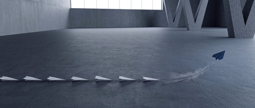 A blue paper plane taking off and flying away from a line of white paper planes in a minimalist concrete industrial room, representing leadership, innovation, and taking a unique direction.