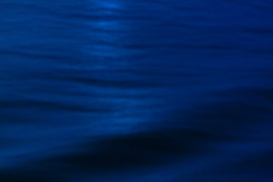 The ocean surface, midnight blue colours in the darkness, reflections and ripples on the water.