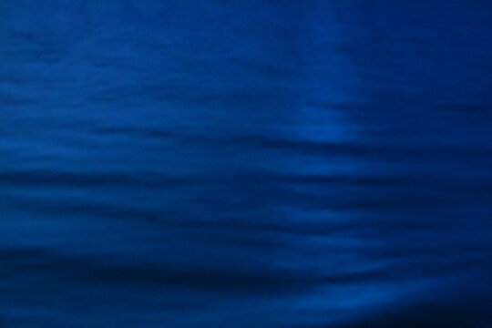 The ocean surface, midnight blue colours in the darkness, reflections and ripples on the water.