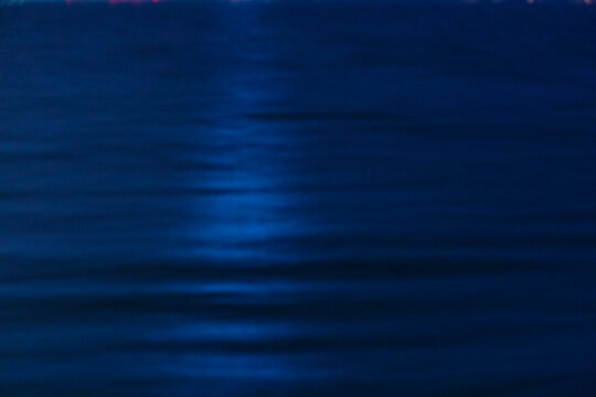 The ocean surface, midnight blue colours in the darkness, reflections, a faint shaft of light on the water.