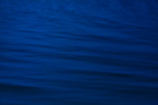 The ocean surface, midnight blue colours in the darkness, reflections, a faint shaft of light on the water.