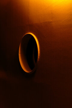 A round window in a wall, a boat deck in darkness with a sliver of light reflection.