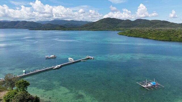Aerial Drone View of a Wooden Pier and Boats in a Turquoise Bay Surrounded by Green Mountains in East Nusa Tenggara Timur, Indonesia