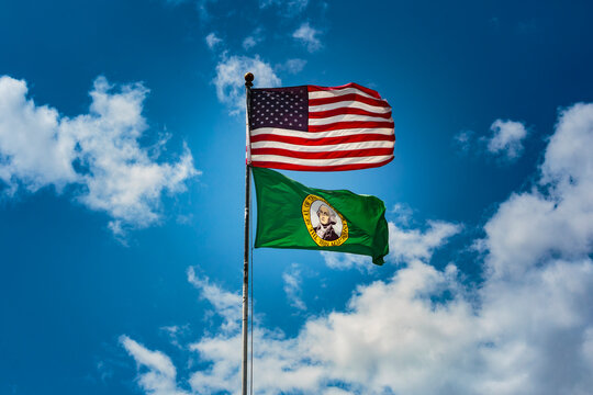 Two flags, US and Washington State Flags on a flag pole with blue sky background.