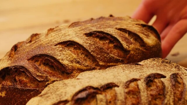 Woman arranges rye bread with beautiful decorative patterns on surface on wooden rack. Baker arranges bread in perfectly straight line