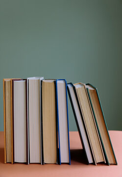 Row of old hardcover books, balancing upright on a shelf.