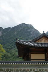 Obraz premium Traditional Korean temple roof in Seoraksan National Park with scenic rocky Seorak mountain peak and cable car line under overcast sky, historical Asian architecture and cultural travel background.