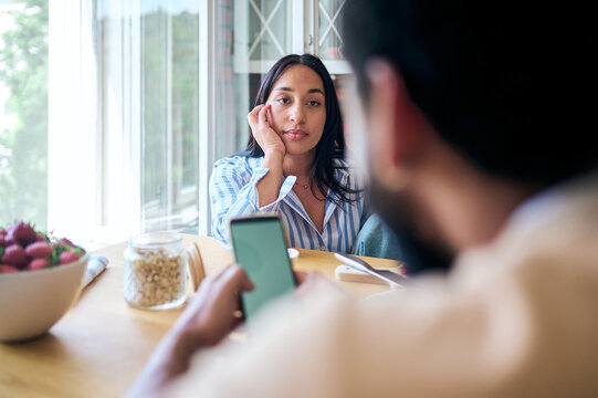 Woman feeling ignored by partner using smartphone during breakfast