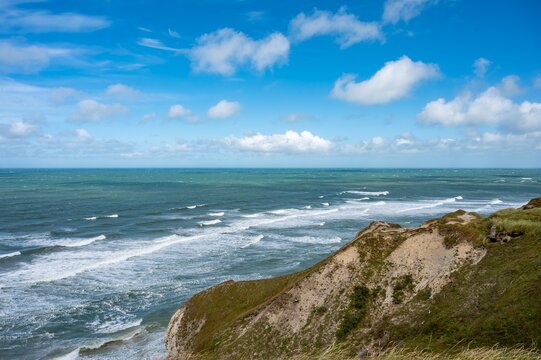 Windswept sea with long rows of whitecaps seen from a grassy dune cliff