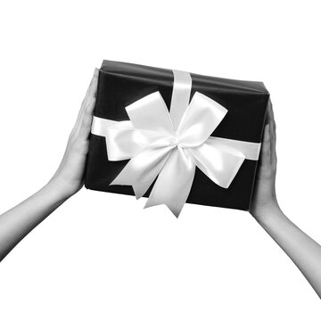 Two hands are holding a black gift box that is decorated with a large white ribbon and bow. The background is transparent and plain.