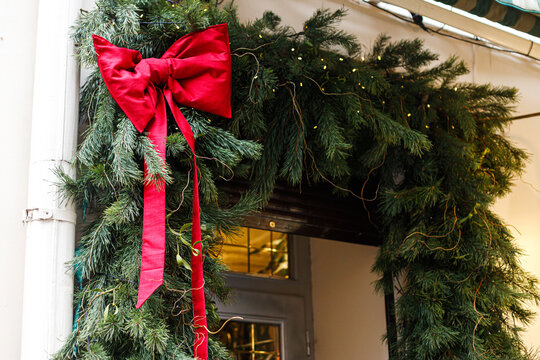 Luxurious pine branch garland featuring a bright red bow and warm glowing fairy lights decorating a classic doorway entrance. Xmas outdoor decor
