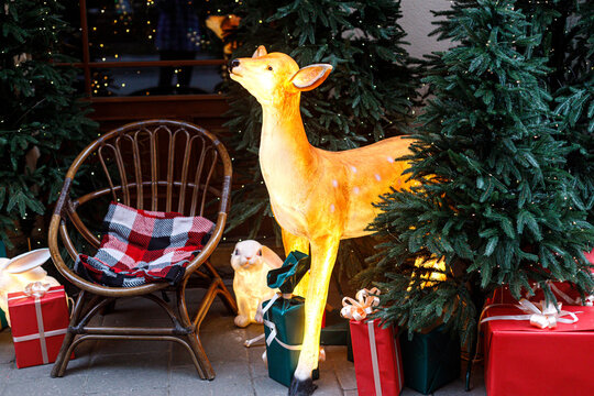 Illuminated reindeer figure with red gift boxes under fir tree outside shopfront. Magical winter Christmas street decoration concept, festive holiday display.