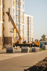 Orange truck-mounted aerial lift with raised boom and empty work basket at a residential construction site beside a modern apartment building © Vasilisa Dorofeeva