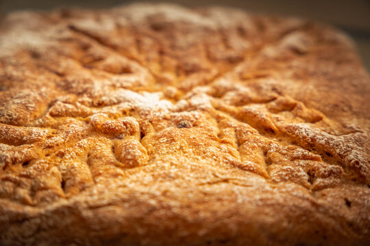 Close view of homemade rye bread with cranberries, showing a dark golden crust, delicate flour dusting, decorative scoring, and scattered berry pieces