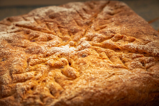 Close-up of homemade rye bread with cranberries, showcasing the richly browned crust, flour-dusted surface, decorative scoring, and baked berry pieces