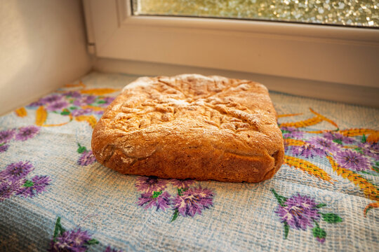 Fresh homemade loaf with a richly browned crust, fine flour dusting, and an intricate wheat-like scoring pattern resting on a colorful kitchen cloth