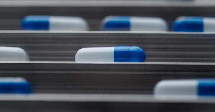 Close-up blue and white pharmaceutical capsule centered on conveyor track for medical factory