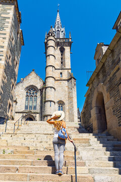 Young female traveler with straw hat climbing stone stairs towards Church of Saint Melaine in Morlaix Brittany France