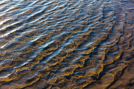 Beach sand formations, created by water action, ripples and ridges, patterns, shallow water and an incoming tide.