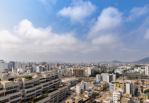 Aerial view of the urban landscape of Lima, featuring dense residential and commercial buildings, modern high-rise architecture, and distant hills in Lima, Callao Region, Peru.
