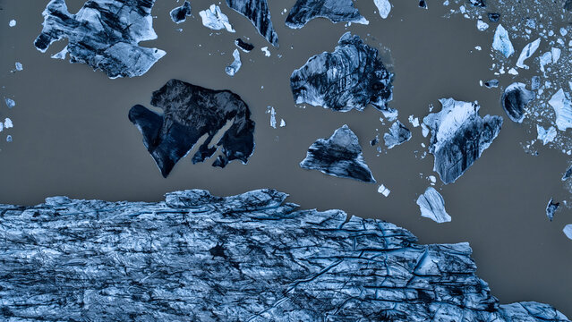 Aerial view of Falljokull glacier with icebergs floating in dark glacial water, showcasing intricate ice textures and deep crevasses in Hofn, Sveitarfelagid Hornafjardar, Iceland.