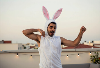 Fototapeta premium Easter celebration and festive fun, young man wearing a white bunny costume dancing on a rooftop terrace during a party at sunset with string lights