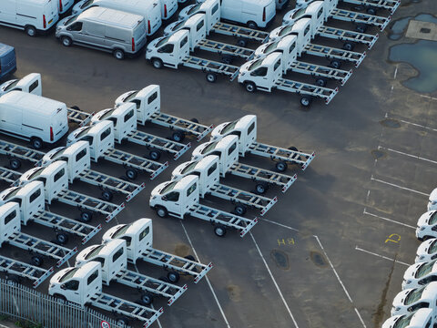 Aerial view of rows of white commercial truck chassis and vans parked in a large outdoor lot in the United Kingdom.
