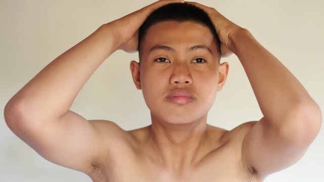 Portrait of Asian teenage boy with buzz cut hairstyle, hands on head against white background