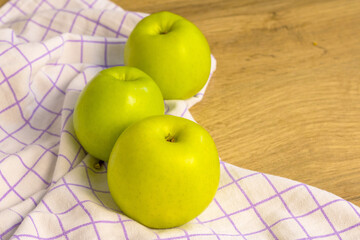 Three green apples arranged on a checkered cloth over a wooden table. Fresh fruit and healthy food lifestyle concept. © Ekaterina Uteva