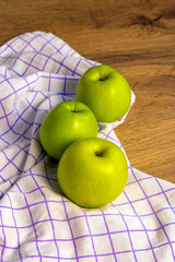 Three green apples arranged on a checkered kitchen cloth over a wooden table. Fresh fruit and healthy eating concept © Ekaterina Uteva