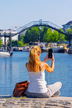 Vertical view of female traveler taking photo with smartphone near river footbridge in Rennes Brittany France