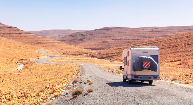 Camper van driving on winding desert road through rocky canyon landscape in Morocco
