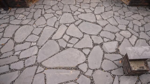 Slow tracking shot over a grey flagstone patio with irregular stones and gravel