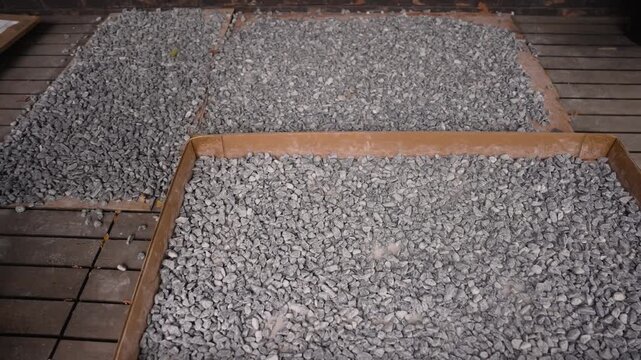 Zooming out from grey crushed stone gravel spread in cardboard tray on wooden deck for construction