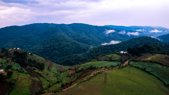 Aerial view of the lush green hills and terraced farmland surrounding the town of Kisoro, with misty mountains in the background under a cloudy sky in Kisoro, Western Region, Uganda.