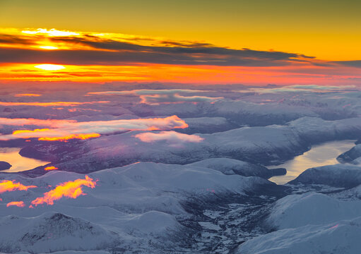 Aerial view of snow-covered mountains and fjords under a vibrant sunset sky in Alesund, More og Romsdal, Norway.