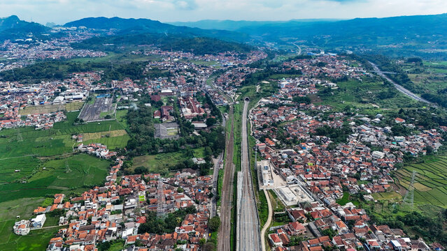 Aerial view of the town of Ngamprah featuring railway tracks, a tunnel entrance, residential neighborhoods, and surrounding rice fields in Ngamprah, West Java, Indonesia.
