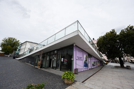 Modern glass shopping pavilion and urban plaza in Radom, Poland with sloped terrace, storefront displays and city square architecture