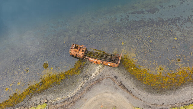 Aerial view of the rusted WWII US Navy LCM ship wreck resting on the rocky shoreline of the fjord in Reydarfjordur, Fjardabyggd, Iceland.