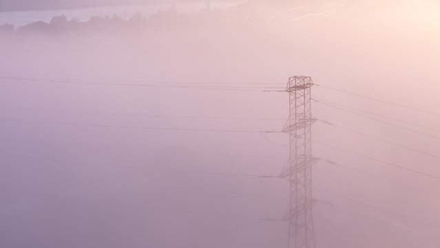 Aerial view of an electricity pylon emerging from thick morning fog during golden hour in Gdansk, Polska.